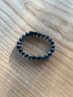 Grått pärlarmband med stenar - Snyggt armband med runda pärlor i olika nyanser av grått och svart. Pärlorna är av sten och sitter på ett elastiskt band, vilket gör det enkelt att ta på och av. Perfekt accessoar för att ge din outfit en cool touch. Jätte snyggt armband. Det är helt nytt!