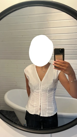 Vit topp med v-ringning från Weekday - Superfin slutsåld topp från weekday! Säljer en vit blus från Weekday i storlek 38. Blusen har v-ringning, knappar framtill och är ärmlös. Den är figurnära med snygga rynkade detaljer längs sidorna som ger en cool siluett.