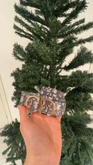 Dior bälte  - Säljer ett snyggt Dior bälte med ikoniskt mönster i mörkblått och grått. Bältet har ett stort, lyxigt guldspänne med CD-logga. Perfekt accessoar för att lyfta din outfit med exklusiv vibe😁🤩