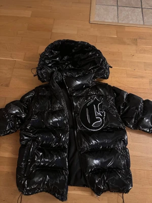 Svart pufferjacka från Corvidae - Säljer en svart glansig pufferjacka från Corvidaes första collection. Jackan säljs inte nå mer och är eftertraktad . Kan bli till en väst med luva eller väst utan luva. Använd i 1 månad sen har den bara legat i garderoben. Finns i morgongåva 