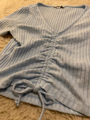 Ljusblå ribbad topp - Supersöt ljusblå topp från Newyorker i ribbad bomull med korta ärmar och v-ringning. Toppen är i XS och har snygg snörning framtill som går att justera och en croppad passform💞