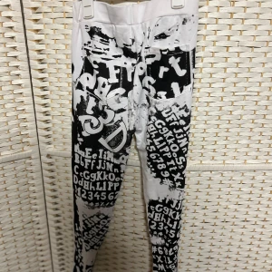 Svarta och vita leggings med bokstavsmönster - Säljer ett par unika leggings i svart och vitt med tryck av bokstäver och siffror över hela byxorna. De har en tight passform och är perfekta för dig som vill sticka ut med din stil. Helt nya. Storlek S.