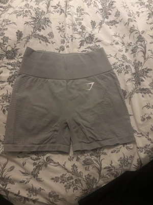 Grå Gymshark seamless shorts - Säljer ett par grå seamless shorts från Gymshark med hög midja och ribbad linning. De har en tight passform och är tillverkade i mjukt, stretchigt material som passar perfekt för träning. Diskret Gymshark-logga framtill och snygga texturdetaljer längs sidorna.
