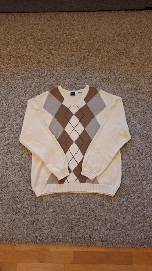 Beige rutig stickad tröja från Arrow - Beige stickad tröja från Arrow i storlek M(passar L också). Använd fåtal gånger och skicket är i princip som ny, inga defekter eller slitningar finns. Den är riktig varm och skön och har rutiga mönster på framsidan. Passar perfekt som en fin julklapp till familjemedlemmar eller för dig som både vill hålla dig stilig och varm nu under vintern och Julen! Skick: 8.5/10