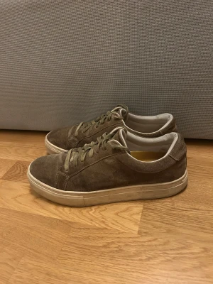 Bruna mockasneakers från Vagabond - Säljer ett par bruna sneakers från Vagabond i mocka med klassisk låg profil och snörning. Skorna har en vit sula och diskret branding på hälen. Perfekta för dig som gillar stilrena och enkla sneakers med en touch av premiumkänsla.