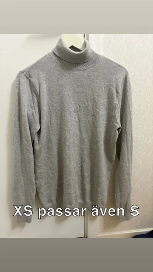 Grå polotröja i mjuk bomull XS/S - Säljer en stilren grå polotröja med lång ärm och ribbad krage. Tröjan är i mjuk bomull och har en klassisk passform som funkar till många outfits. Perfekt för lager-på-lager under kyliga dagar.