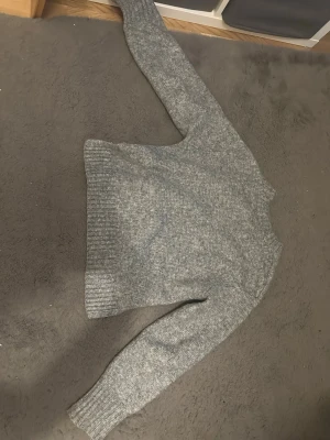 Pris kan diskuteras  - Mysig grå stickad tröja med rund hals och ribbade muddar vid ärmslut och nederkant. Perfekt för kyliga dagar och enkel att matcha med jeans eller andra favoritplagg. Klassisk modell med lång ärm och mjukt material.