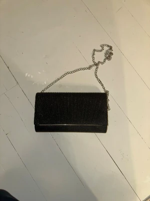 Svart glittrig handväska med kedja - Snygg svart habdväska med glittrigt tyg och silverfärgad kedja. 
