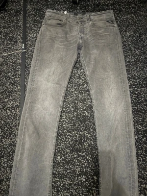 Replay grå jeans med smal passform - Snygga grå jeans från Replay med klassisk femficksdesign och smal passform. Jeansen har en diskret tvättad look och svarta Replay-detaljer vid fickan. Perfekt för dig som gillar stilrena och moderna jeans med lite edge.