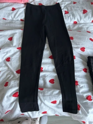 Svarta leggings från Zaroni Club - Svarta leggings från Zaroni Club i storlek 152. De har en elastisk midja och är tillverkade i mjukt material som sitter tight mot benen. Perfekta att matcha med en oversized hoodie eller t-shirt för en chill look.