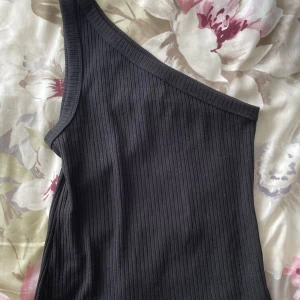 One shoulder topp - Cool one shoulder topp från Kappahl i svart randigt tyg😍Använt mycket och är väldigt skön. Kommer inte till användning längre tyvärr. Storlek S, sitter tajt men är stretchig. Skriv för bilder och frågor💕💕
