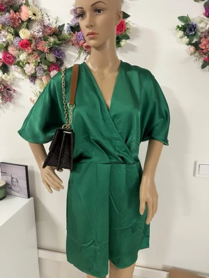 Grön omlott byxdress i satinlook ZARA  - Snygg grön byxdress med omlottliv och vida, korta ärmar. Materialet har en satinliknande glans och känns mjukt mot huden. Perfekt för dig som vill sticka ut med en färgstark och trendig look.