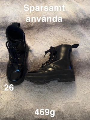 Svarta boots med snörning, storlek 26 - Säljer ett par svarta boots med snörning och grov sula. Skorna har en blank finish och metallöglor för snörena. Praktisk dragflik baktill och rund tå. Perfekt för dig som gillar chunky stil och vill ha något som sticker ut.🌸Sparsamt använda. Storlek 26 