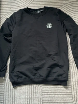 Svart Trapstar sweatshirt XL - Säljer en svart sweatshirt från Trapstar i storlek XL. Tröjan har rund hals, lång ärm och Trapstar-logga på bröstet samt stor text på ryggen. Tillverkad i mjuk bomull med lite stretch för extra komfort. Perfekt för dig som gillar streetwear.