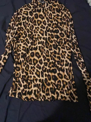 Leopardmönstrad långärmad polotopp - Säljer en snygg långärmad polotopp med leopardmönster i beige, brunt och svart. Toppen har en smickrande slim passform och är perfekt för dig som vill sticka ut med ett djuriskt print. Materialet känns mjukt och följsamt mot kroppen.