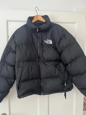 Svart pufferjacka från The North Face - Säljer en svart pufferjacka från The North Face, modell 700. Jackan har hög krage, dragkedja framtill och två sidofickor med dragkedja. Klassisk logga på bröstet och ärmen. Perfekt för kalla dagar och riktigt snygg oversized look.