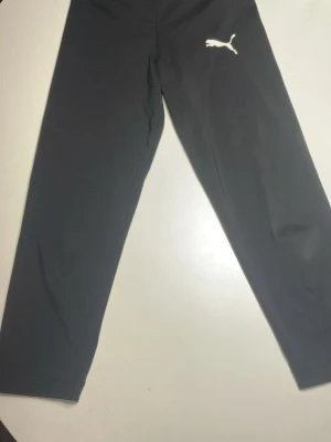 Svarta tränings byxor från Puma - Svarta tränings byxor från Puma med klassisk vit logga på låret. Byxorna har rak passform och är tillverkade i mjukt bomullsmaterial som är sköna att ha på sig hela dagen. 