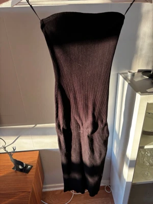 Svart ribbad långklänning H&M - Säljer en svart ribbad långklänning från H&M utan axelbanf och figurnära passform. Klänningen är ärmlös och har en enkel, stilren design som passar perfekt till många olika tillfällen. Materialet är stretchigt och bekvämt.