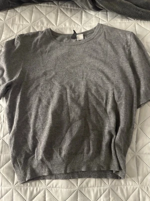 Grå stickad topp med kort ärm - Fin grå basic tröja med kort ärm från HM. Är i storlek L men är väldigt liten så passform skulle jag säga är nog S.