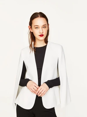 Vit kavaj från Zara Woman - Säljer en stilren vit kavaj från Zara Woman med öppen front och raka linjer. Kavajen har en modern cape-liknande design med slitsar vid ärmarna och två fickor framtill. 