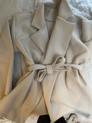 Beige kappa  - Säljer en populär och fin jacka/kappa från missay! Den har tecken på användning men är fortfarande fin. Den kommer med ett skärp. Storleken står inte men skulle gissa på xs-s. 