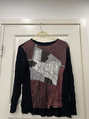 Långärmad vintage topp från Zara Collection - Säljer en långärmad vintage topp från Zara Collection i storlek L. Toppen har svart bas med ett grafiskt mönster i vinrött, grått och vitt framtill. Materialet är mjukt och stretchigt, perfekt för dig som gillar unika prints och bekväma plagg.