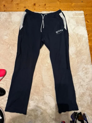  Hugo Boss mjukis - Snygga mörkblå mjukisbyxor från Hugo Boss med vita detaljer vid fickorna och vit snörning i midjan. Loggan har lossnat lite men annars bra skick