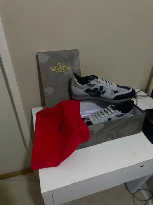 Valentino Garavani Rockrunner sneakers - Säljer ett par Valentino Garavani Rockrunner sneakers i svart, grått och vitt med snyggt camouflage-mönster. Skorna har snörning, rund tå och platt sula. Kommer med originalkartong och röd dustbag. Perfekta för dig som gillar exklusiva sneakers med unik design.