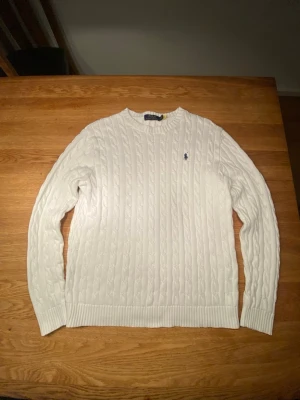 Vit kabelstickad tröja Polo Ralph Lauren - Vit kabelstickad tröja från Polo Ralph Lauren i bomull. Klassisk rund halsringning och långärmad modell med den ikoniska blå broderade loggan på bröstet. Perfekt för dig som gillar stilrena och tidlösa plagg.            Jag kan alltid förhandla priset! 