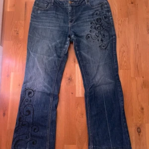 Blå jeans med svart mönster - Unika blå jeans med svarta swirl-mönster på framsidan av benet och höften samt broderade detaljer på bakfickorna. egengjorda