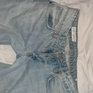 Ljusblå raka jeans med låg midja, low baggy  - Säljer ett par ljusblå jeans med låg midja och raka ben. Klassisk femficksmodell med bälteshällor och knappgylf. Jeansen har en avslappnad vibe och är perfekta för dig som gillar en enkel och stilren look. Från Zara i storlek 34 