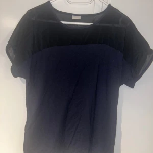 Topp - Snygg svart topp med transparent mesh upptill. Rund halsringning och korta ärmar ger en stilren look. Perfekt för dig som gillar en enkel men trendig stil.