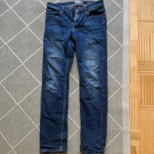 Blå jeans från Dressmann 31/32 - Säljer ett par klassiska blå jeans från Dressmann i storlek 31/32. Jeansen har rak passform, fem fickor och snygga slitningar på benen. Perfekta för dig som gillar en tidlös look med lite edge.