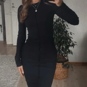 Svart ribbad långklänning från Nelly - Supersnygg svart långklänning från Nelly i ribbad stretchig bomull. Klänningen har lång ärm, rund hals och figurnära passform som framhäver siluetten. Perfekt för dig som gillar minimalistisk och stilren look.