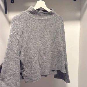 Grå polotröja från Pull&Bear - Mysig grå polotröja från Pull&Bear i storlek XS. Tröjan har en hög krage, ribbade muddar och är tillverkad i ett mjukt stickat material. Perfekt för lager-på-lager under kyliga dagar.