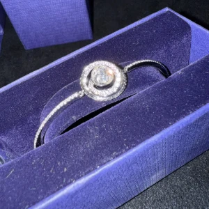 Glittrigt armband med stor kristall - Snyggt armband i silverfärg med en stor rund glittrande kristall i mitten, omgiven av mindre stenar i en cirkelformad design. Tunt och elegant band med gnistrande detaljer, perfekt för dig som gillar att sticka ut med dina accessoarer. Vid köp av två eller fler får du dessutom välja en present 🎁❤️ (presenterna kan jag visa i DM eftersom de inte finns upplagda här).