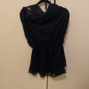 Mörkblå halterneck med volang från Vero Moda - Supersnygg mörkblå blus från Vero Moda med volangkant nertill och knytning i halsen. Blusen har en öppen ryg och har ett lätt, luftigt tyg som ger en flowy känsla. Perfekt för dig som gillar en feminin och trendig look. Köpt second hand så stolekslappen är bortklippt men tycker att den passar som M (men blev tillsagt att de var S). Aldrig använt av mig och kunder inte lämna tillbaks (eftersom att den är second hand)💘💘