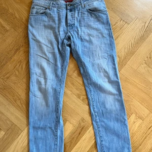 Ljusblå jeans från Jacob Cohen 34 - Säljer ett par ljusblå jeans från Jacob Cohen med klassisk femficksdesign och snygga detaljer som broderad logga på fickan och patch bak. Jeansen har raka ben och normal passform, perfekta till en avslappnad stil. Materialet är mjukt denim i bomull. Inga defekter eller hål och väldigt bra skick. Storlek 34 och det är bara höra av er vid frågor