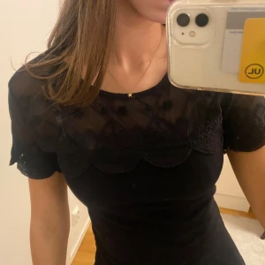 Svart t-shirt med mesh/spets  - Supersnygg svart topp från H&M med transparent mesh upptill och broderade spetsdetaljer. Blusen har korta ärmar och rund halsringning. 