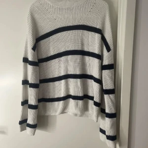 Randig stickad tröja från Kappahl - Säljer en vit stickad tröja från Kappahl i storlek S med svarta horisontella ränder. Tröjan har en loose passform, rund halsringning och långa ärmar. Perfekt för kyliga dagar och enkel att styla med jeans eller kjol.