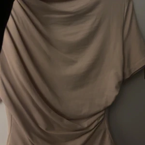 Beige omlott blus med drapering - Säljer en beige omlott blus med snygg drapering framtill. Blusen har korta ärmar och en mjuk, följsam passform som ger en cool och avslappnad look. Perfekt för dig som gillar stilrena och enkla plagg med en twist.