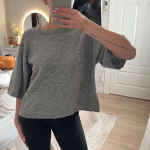 Grå stickad tröja från 157 - Mysig grå stickad tröja från 157 med avslappnad passform och trekvartsärm. Perfekt för lager-på-lager och chill dagar. Enkel design med rund halsringning och mjukt material som känns skönt mot huden.