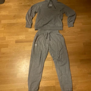 Grå mjukisbyxor från Under Armour - Gråa mjukisbyxor från Under Armour med resår och snörning i midjan. Byxorna har en avslappnad passform, muddar vid bensluten och en liten vit logga på låret. Perfekta för chill eller träning, tillverkade i mjukt bomullsmaterial.Använd flera gånger men inga tecken på det.Storlek S i herr.