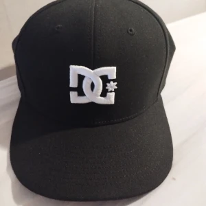 Svart DC Shoes keps med broderad logga - Säljer en svart keps från DC Shoes med vit broderad DC-logga framtill och justerbar snapback baktill. Kepsen är tillverkad i polyester och bomull, har klassisk form och passar perfekt för en streetwear-look. Använd några gånger