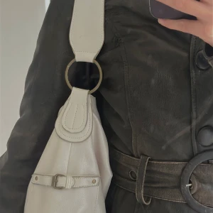 Vit axelväska med metallringar - Snygg vit axelväska i skinn med bred axelrem och stora metallringar antik mässing. 