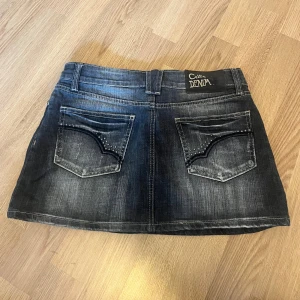 Grå jeanskjol - Supersnygg minikjol som har en ”distressed” look, med en massa coola silver detaljer. Köptes vintage, passar ca S-M.