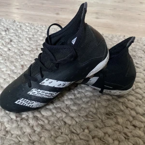 Adidas Predator svarta fotbollsskor - Säljer ett par fina svarta Adidas Predator fotbollsskor i storlek 38 med vita detaljer och mönstrade ränder. SUPER BRA PRIS, köpta för ungefär 1 000.Skorna har snörning, högre skaft och platt sula med dobbar för gräsplan. Bra skick bara lite slitna under till som man kan se på bild fyra men inget som syn på. Hör av dig om du har frågor eller funderingar!