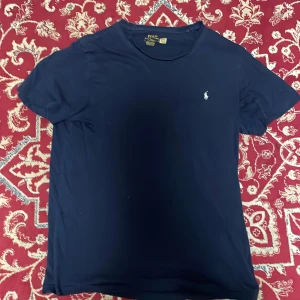  t-shirt Polo Ralph Lauren - Snygg marinblå t-shirt från Polo Ralph Lauren med klassisk rund hals och korta ärmar. T-shirten har den ikoniska broderade loggan i vitt på bröstet och är gjord i mjuk bomull för skön komfort. Perfekt för en clean och stilren look.