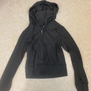 Mörkgrå hoodie med dragkedja - Mörkgrå hoodie med hel dragkedja framtill och två fickor. Tröjan har huva med snörning och långa ärmar. Tillverkad i mjukt material som känns skönt mot huden. Storlek L men passar även M