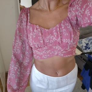 Blus/croptop 36 - Kort topp från Bubbleroom i rosa mönstrat tunt tyg, liknande chiffong. Smockad baksida med resår som gör den töjbar. Använd några få tillfällen men finns inga skavanker eller tecken på användning. 100% polyester 